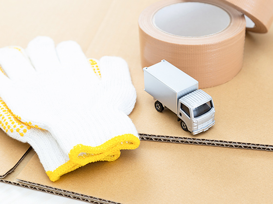 組み立て前の段ボールの上に軍手とガムテープとトラックのトミカを並べた画像